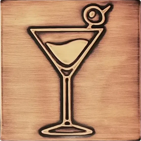 A glass of martini with olive on copper tile